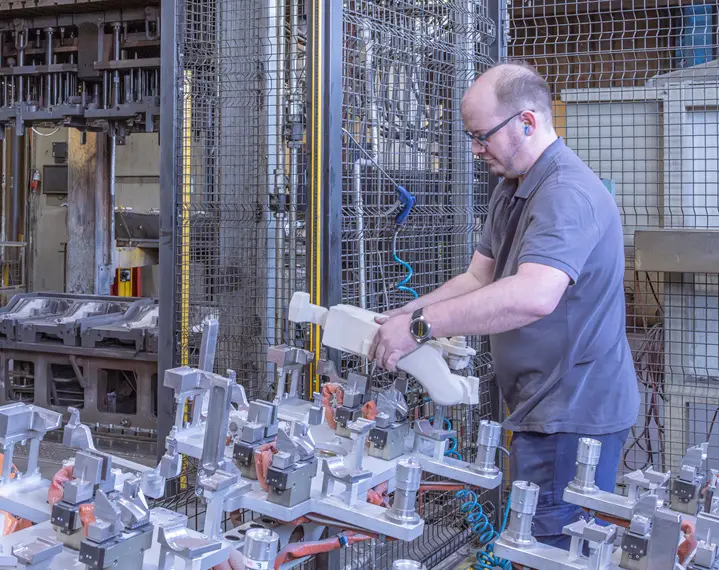 Mann in grauem Poloshirt bedient Maschine in industrieller Fertigungsumgebung mit Metallteilen
