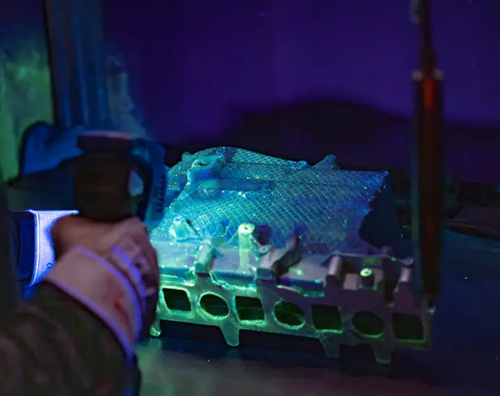 Hand hält ein Messgerät auf ein metallisches Bauteil mit mehreren Öffnungen und einer strukturierten Oberfläche