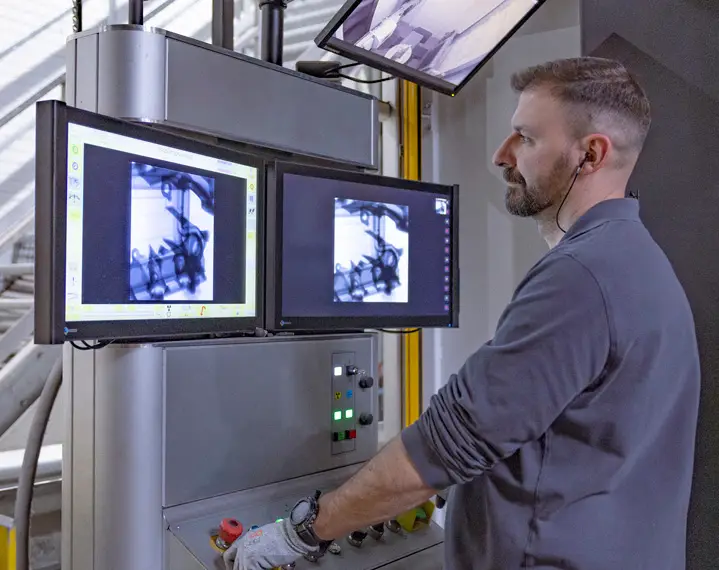 Mann mit kurzem Haar und grauem Pullover bedient eine Maschine mit zwei Bildschirmen, die technische Zeichnungen anzeigen