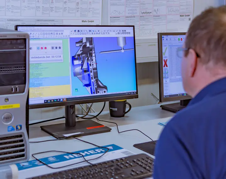 Person sitzt vor zwei Bildschirmen mit technischer 3D-CAD-Zeichnung und Softwarefenstern in einem Büro